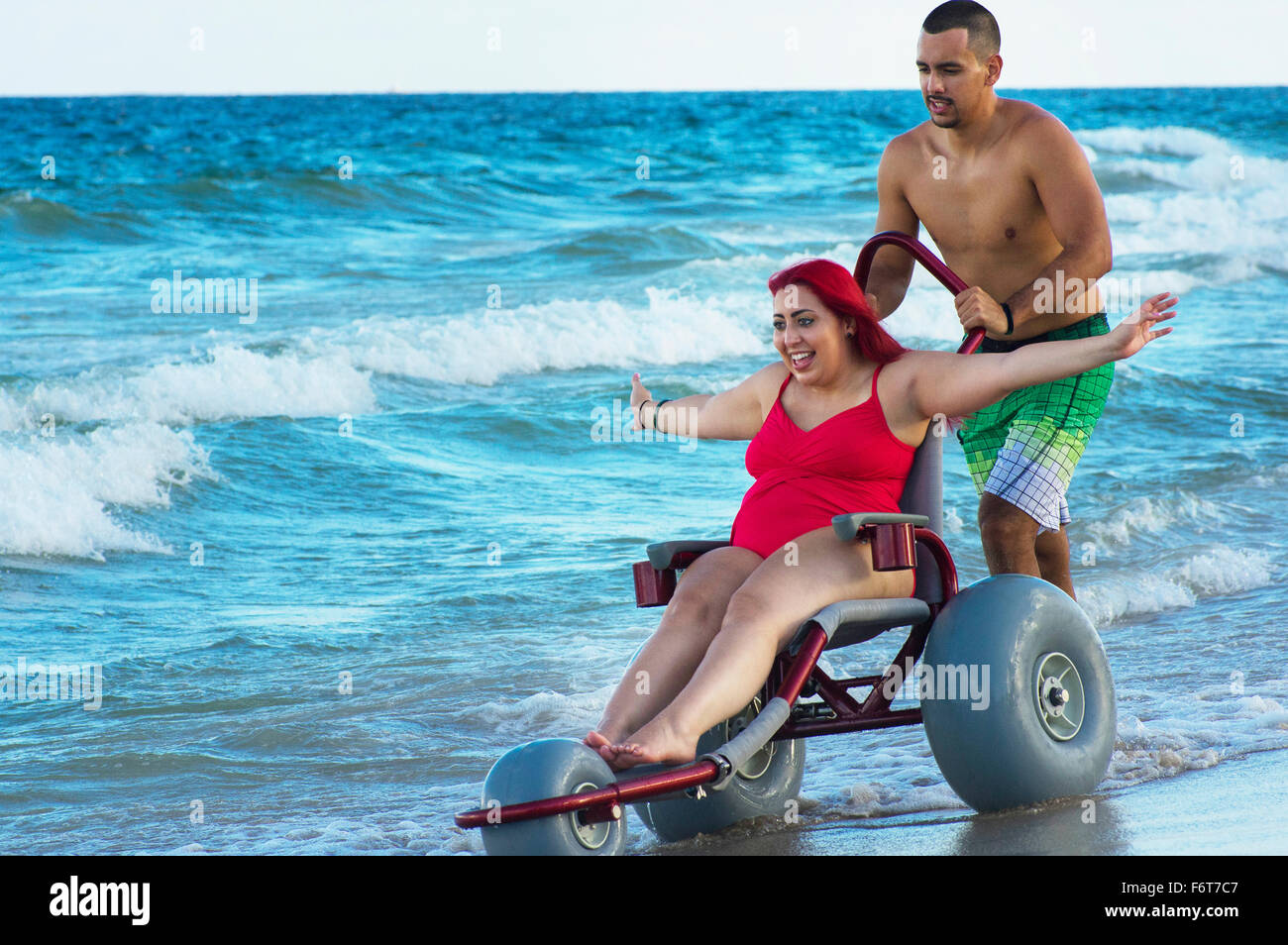 Uomo paraplegico di spinta ragazza in sedia a rotelle sulla spiaggia Foto Stock