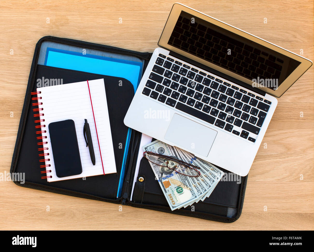 La cartella con i documenti aziendali, un laptop di un notebook con una penna, smartphone e le fatture del dollaro. Vista dall'alto su un tavolo di legno. Foto Stock