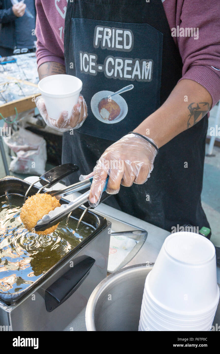 Giovane uomo ascensori palla dorata di Fritto gelato fuori di una friggitrice a fiera di strada su Broadway chiuse al traffico in autunno sabato Foto Stock