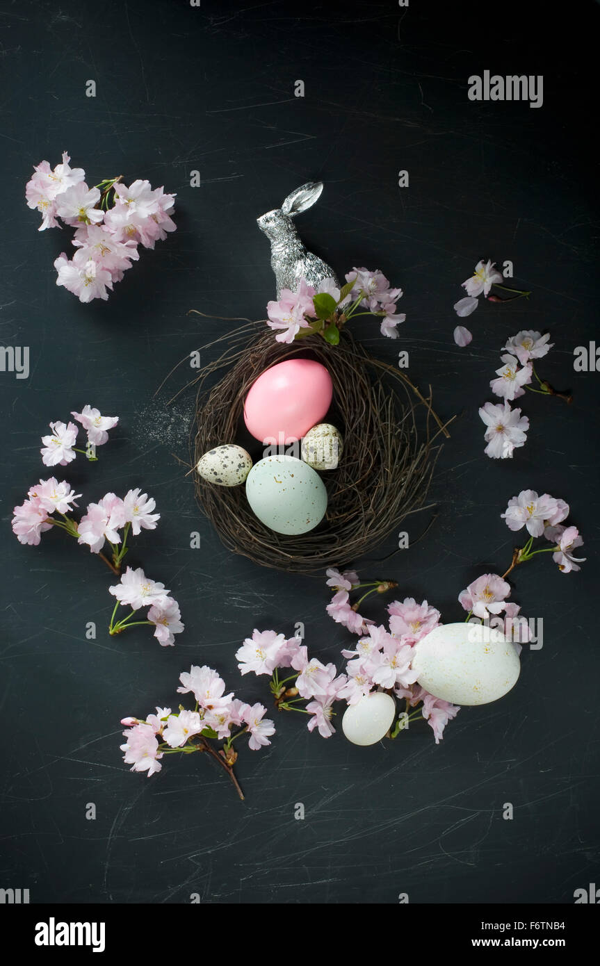 Nido di pasqua con le uova di pasqua, argento coniglietto di Pasqua, piume e fiori di ciliegio Foto Stock