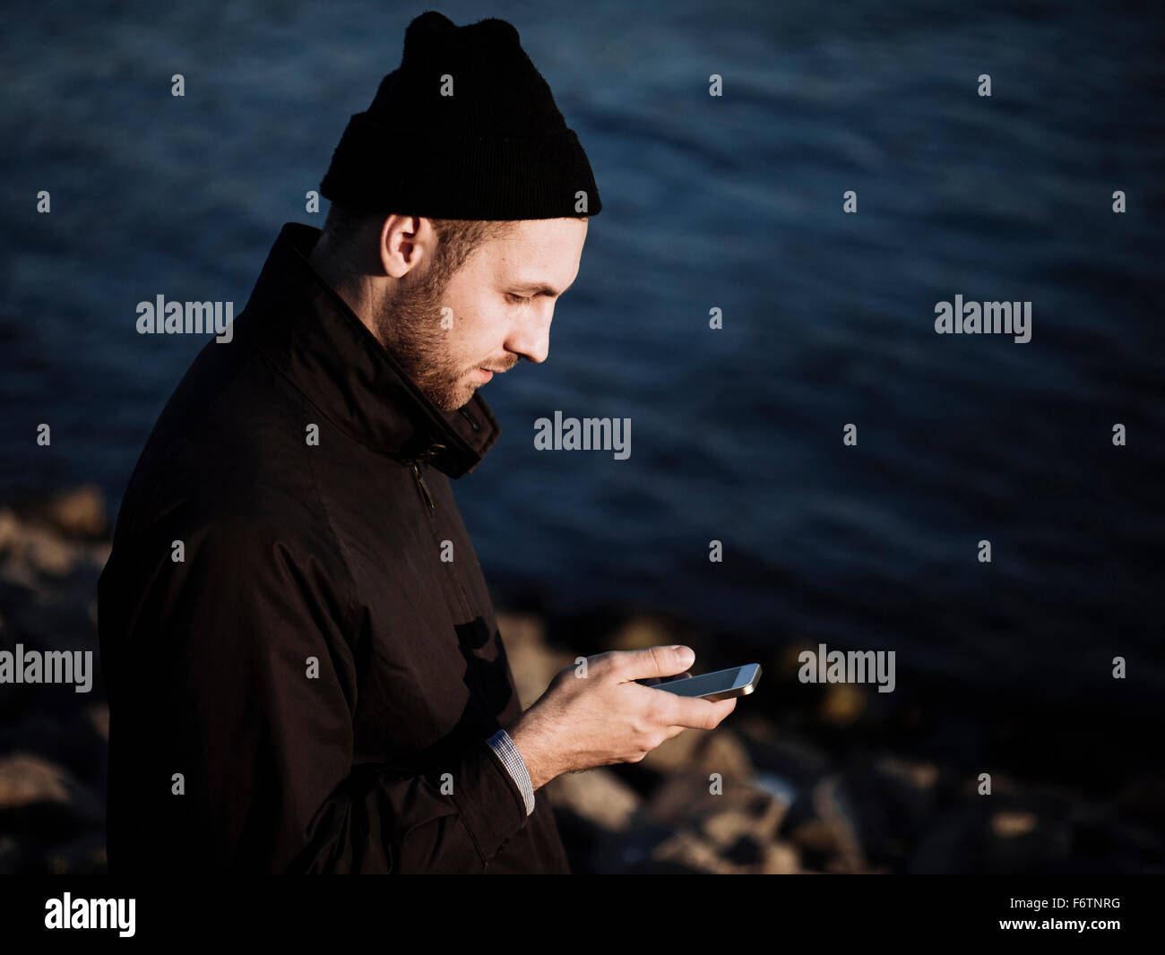 Germania, Colonia, uomo che indossa la moda autunno in piedi nella parte anteriore del fiume Reno con il suo smartphone Foto Stock