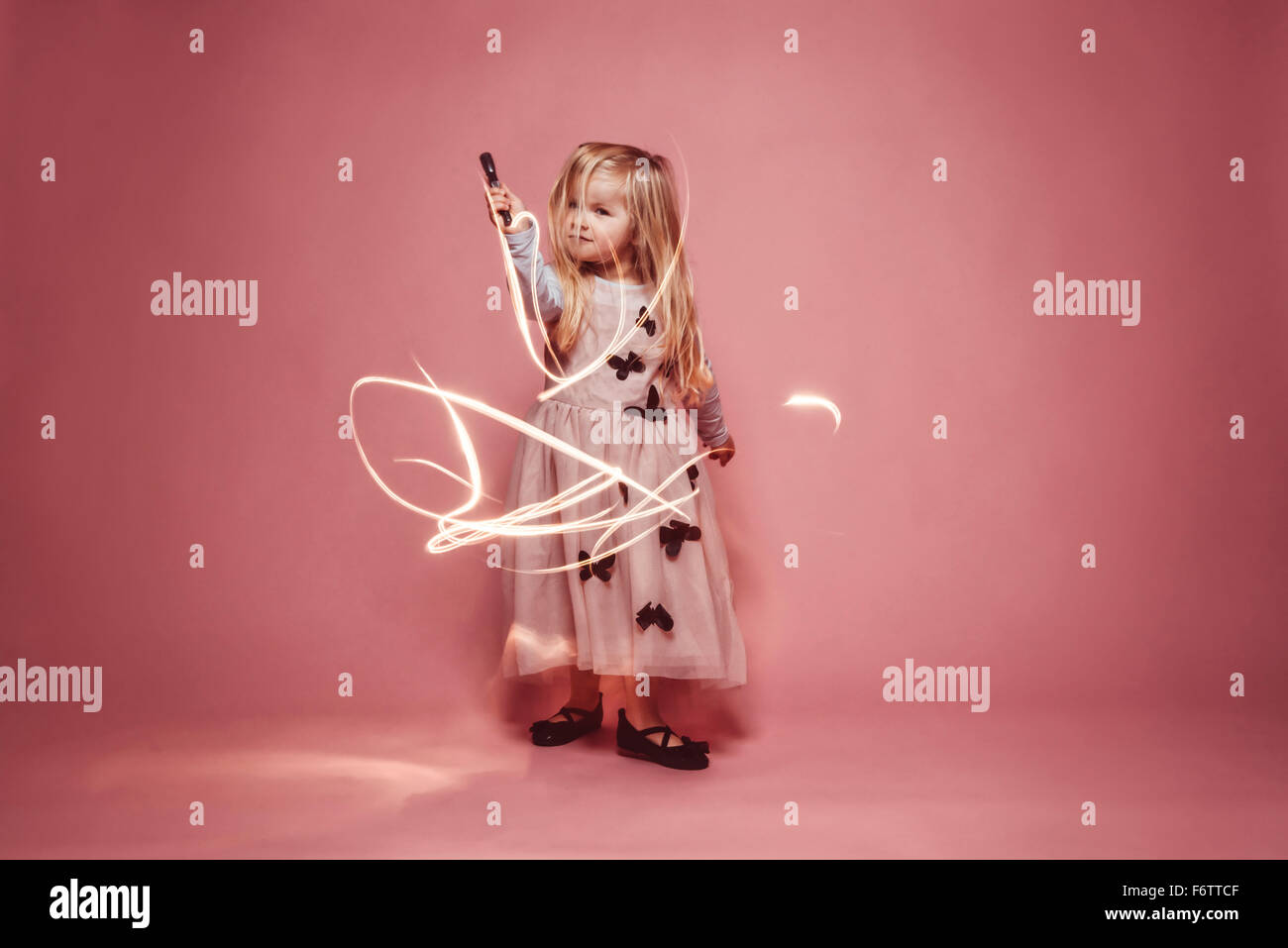 Bambina lightpainting con una torcia nella parte anteriore di uno sfondo rosa Foto Stock