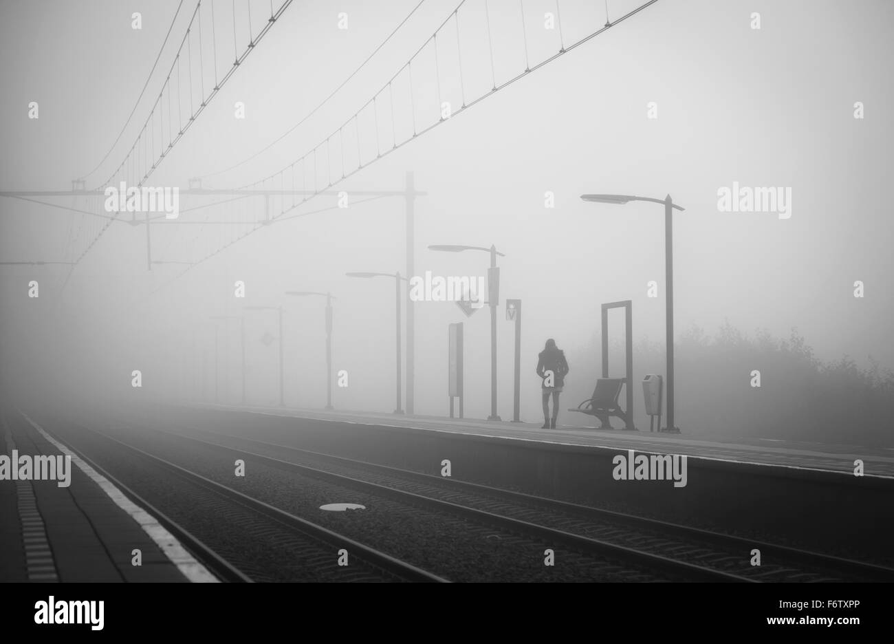 Anonimo donna da sola a una stazione ferroviaria, attesa per il treno in un giorno di nebbia in autunno. Foto Stock