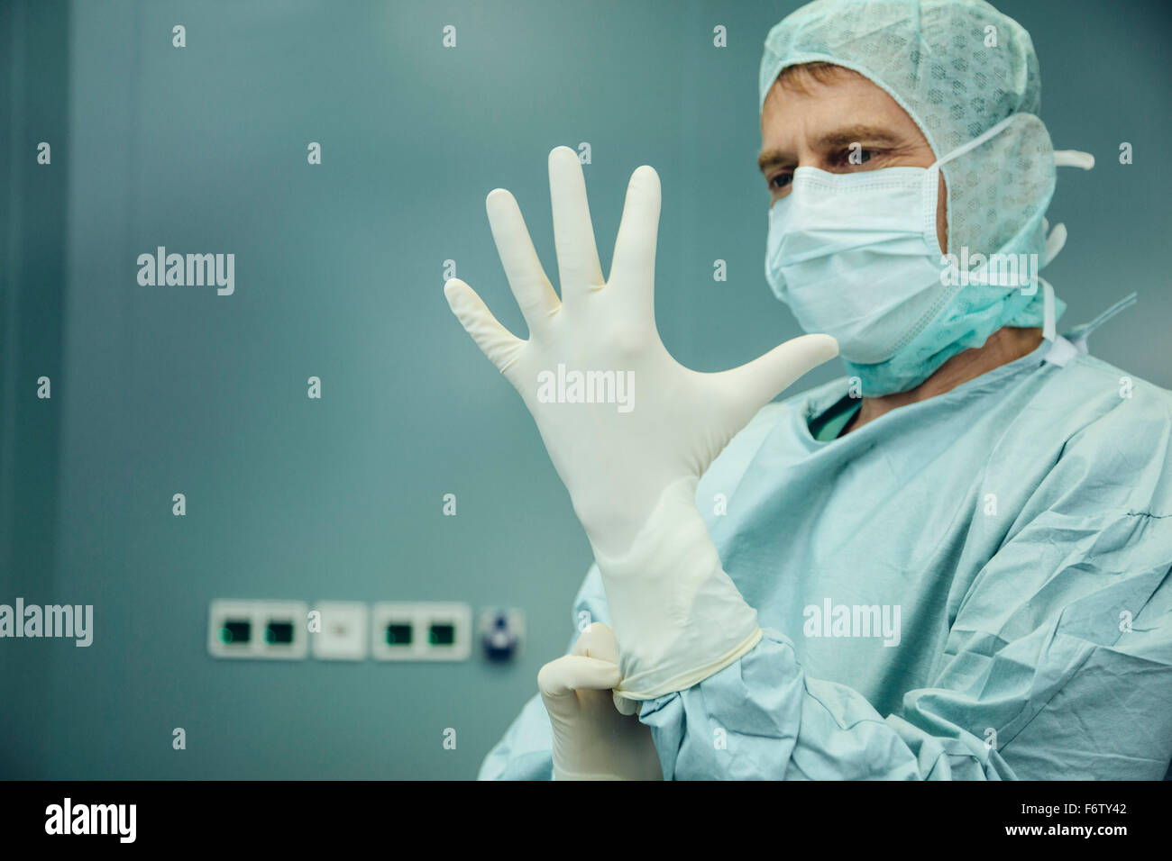 Chirurgo mettendo su guanti chirurgici Foto Stock
