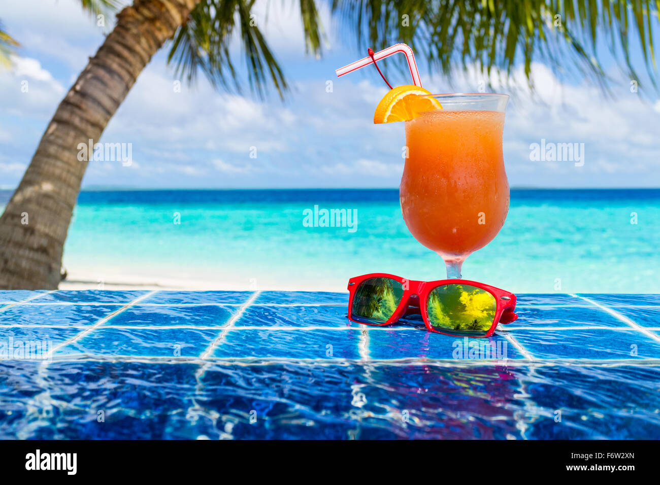 Cocktail di arancione e occhiali da sole, sul bordo della piscina a sfioro Foto Stock