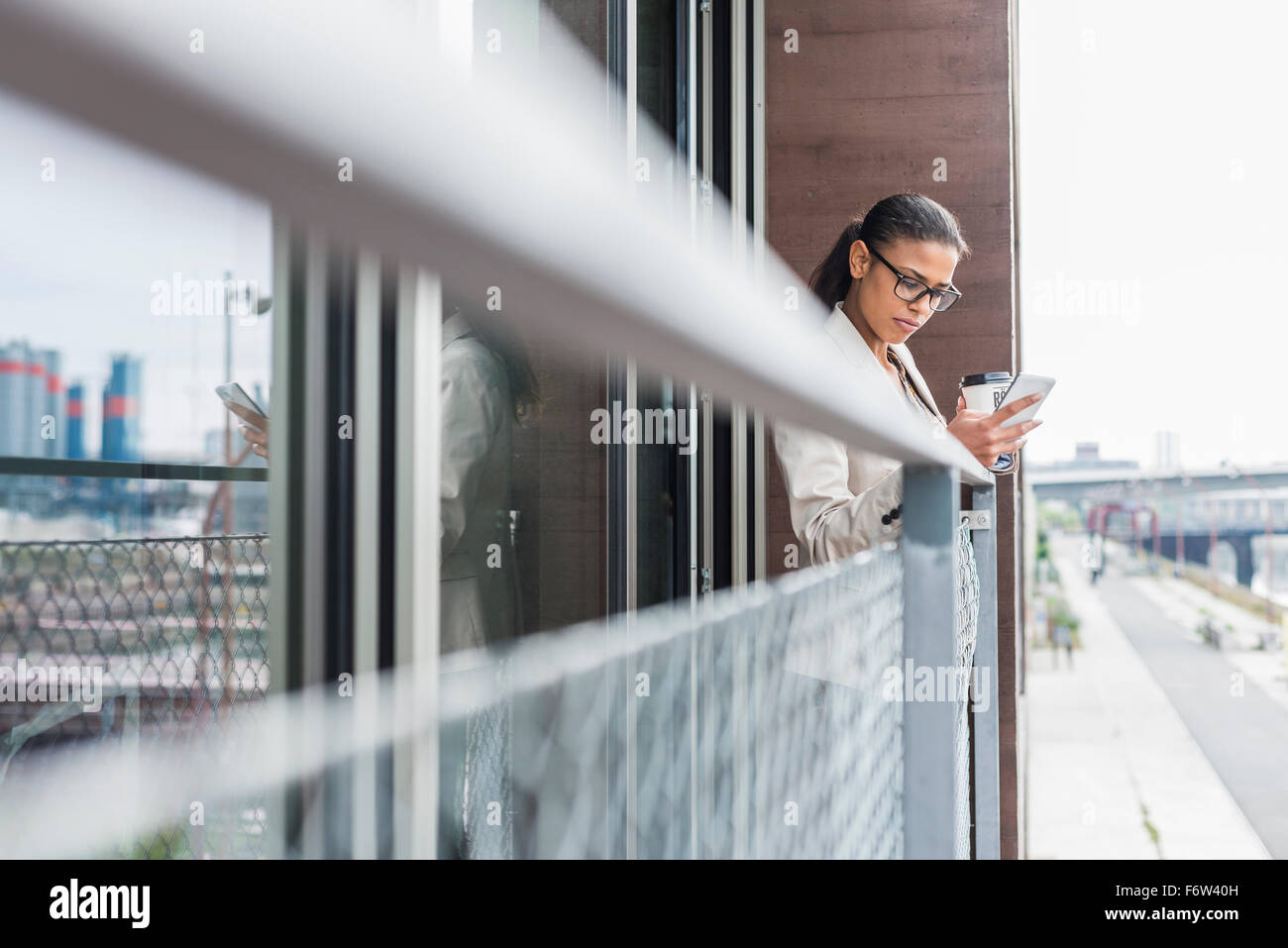 Giovane donna sul balcone con caffè di andare e il telefono cellulare Foto Stock