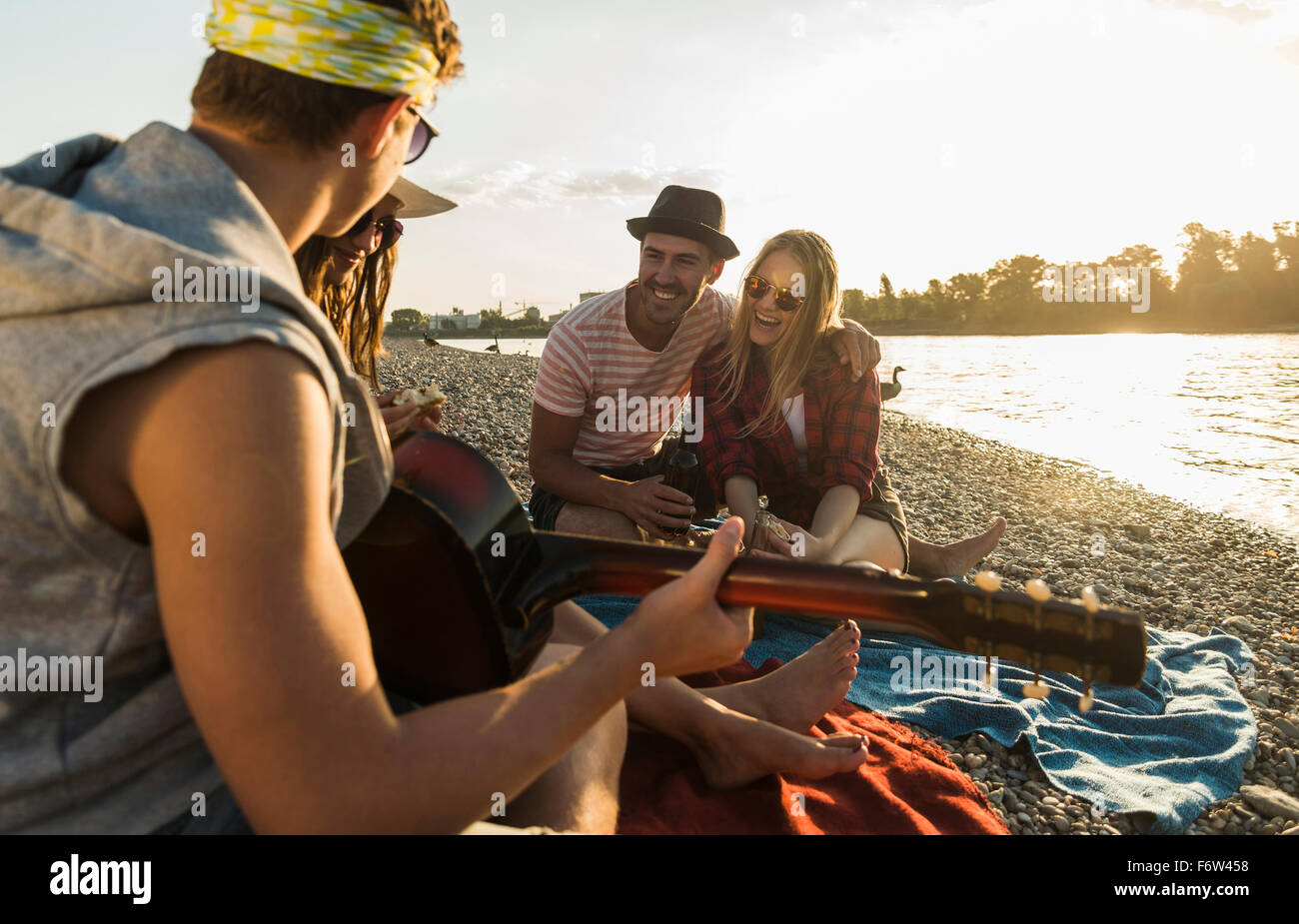 Amici con chitarra rilassante in riva al fiume e al tramonto Foto Stock