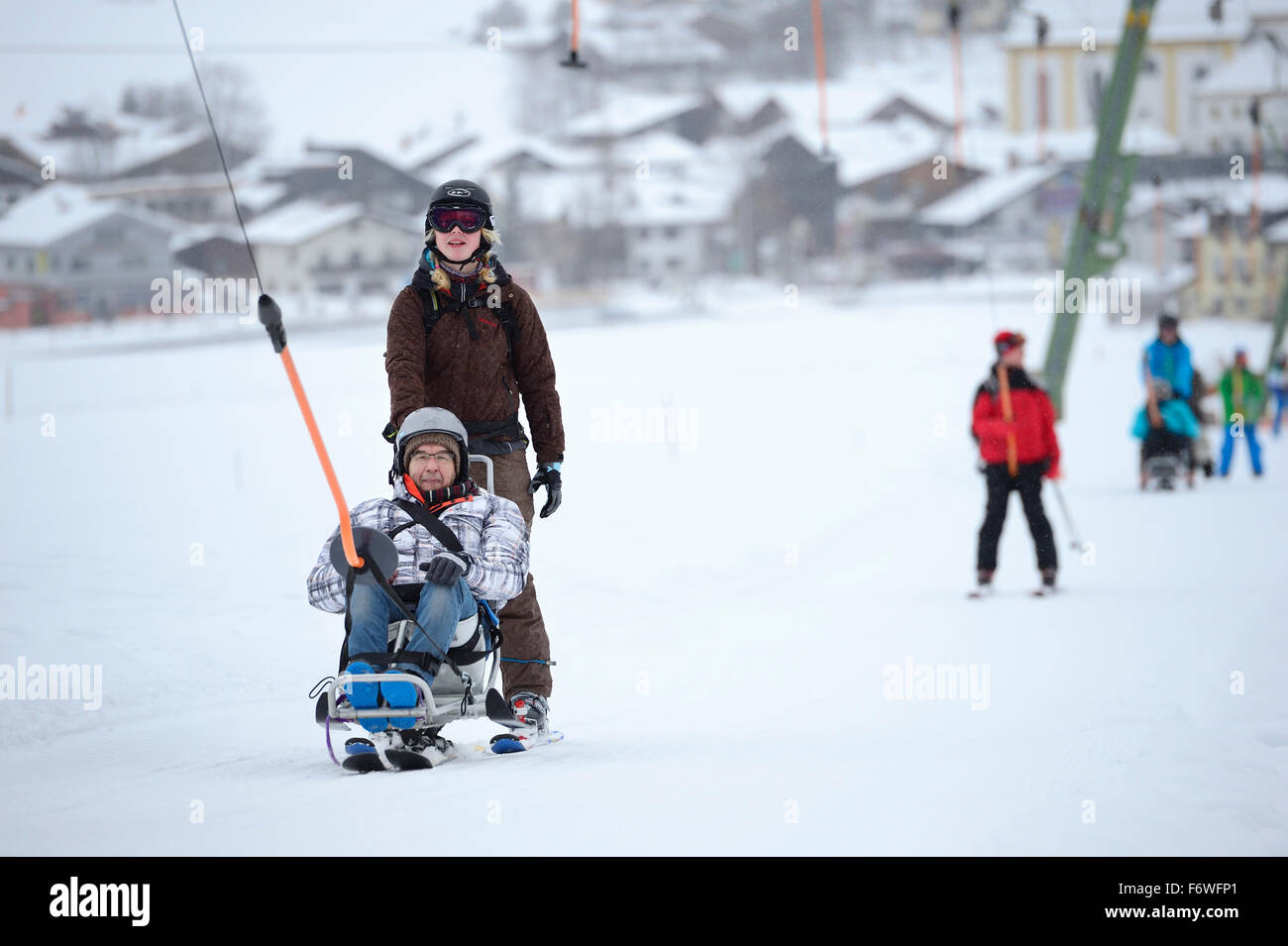 Uomo con disabilità a piedi salendo insieme con operatore con T-bar ascensore, Soell, Kitzbuehel gamma, Tirolo, Austria Foto Stock