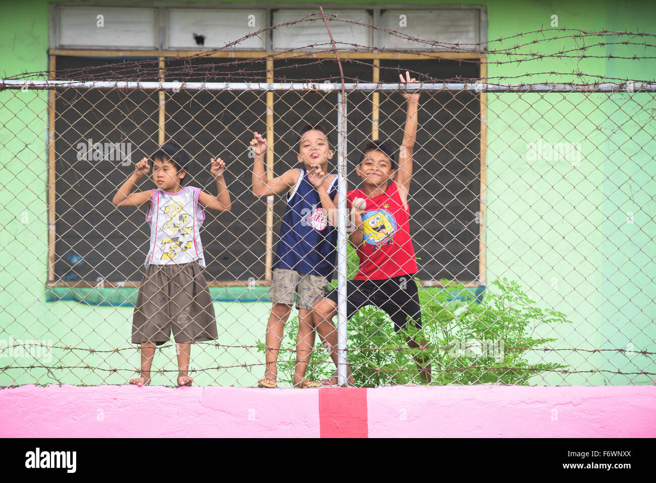 Tre ragazzi guardando attraverso il recinto di filo di Dadiangas South Central Elementary School in General Santos City Foto Stock