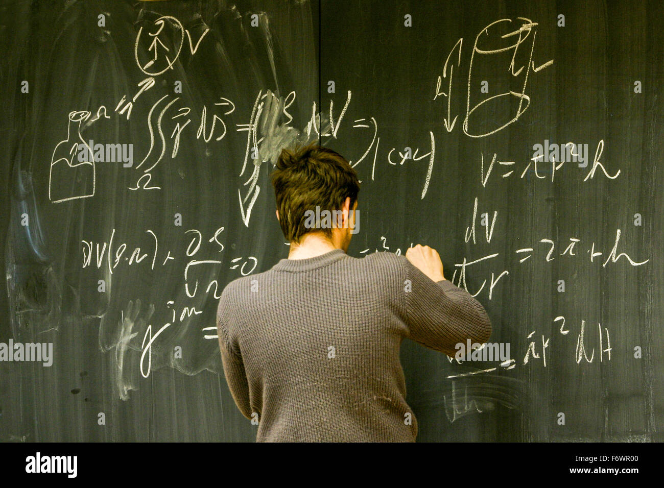 Un adolescente a scuola, vista posteriore, calcolo dell'esempio su una lavagna, scuola di lavagna, esame di matematica, test solving Foto Stock