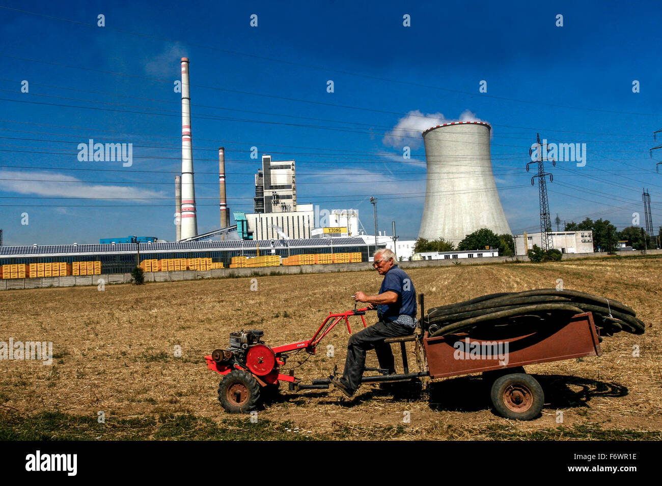 Uomo su un campo agricolo di piccoli trattori, centrale termoelettrica di fondo, Melnik, Boemia centrale, Repubblica Ceca Foto Stock