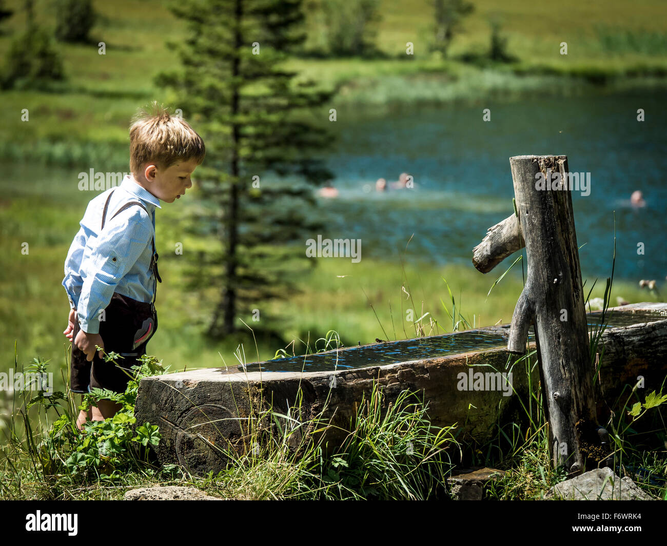 Ragazzo che guarda in una fontana, Lauenen Lago sullo sfondo, Gstaad, cantone di Berna, Svizzera Foto Stock