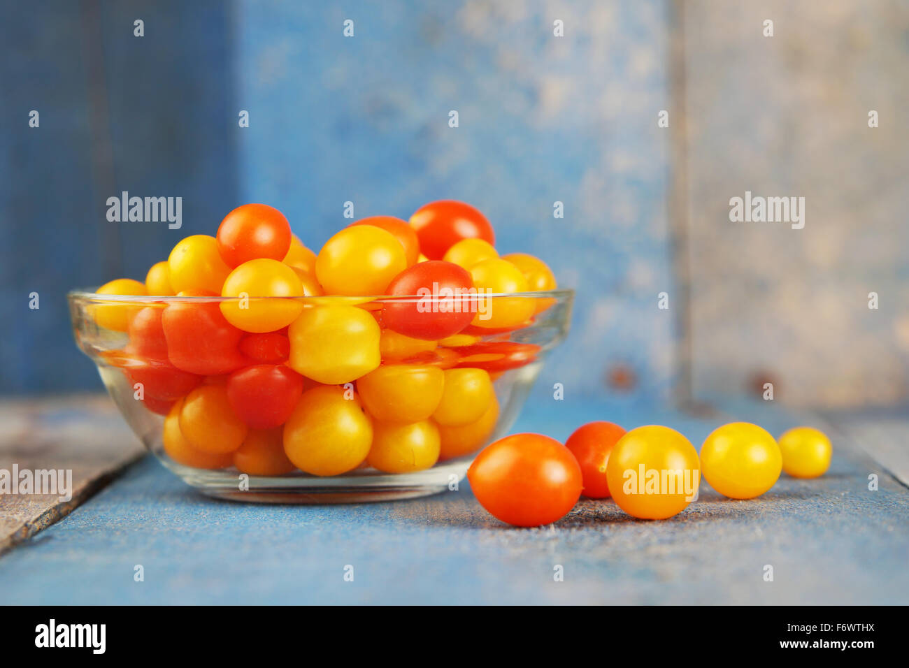 Piccole caramelle colorate di rosso e di giallo pomodori su un vecchio legno blu Foto Stock