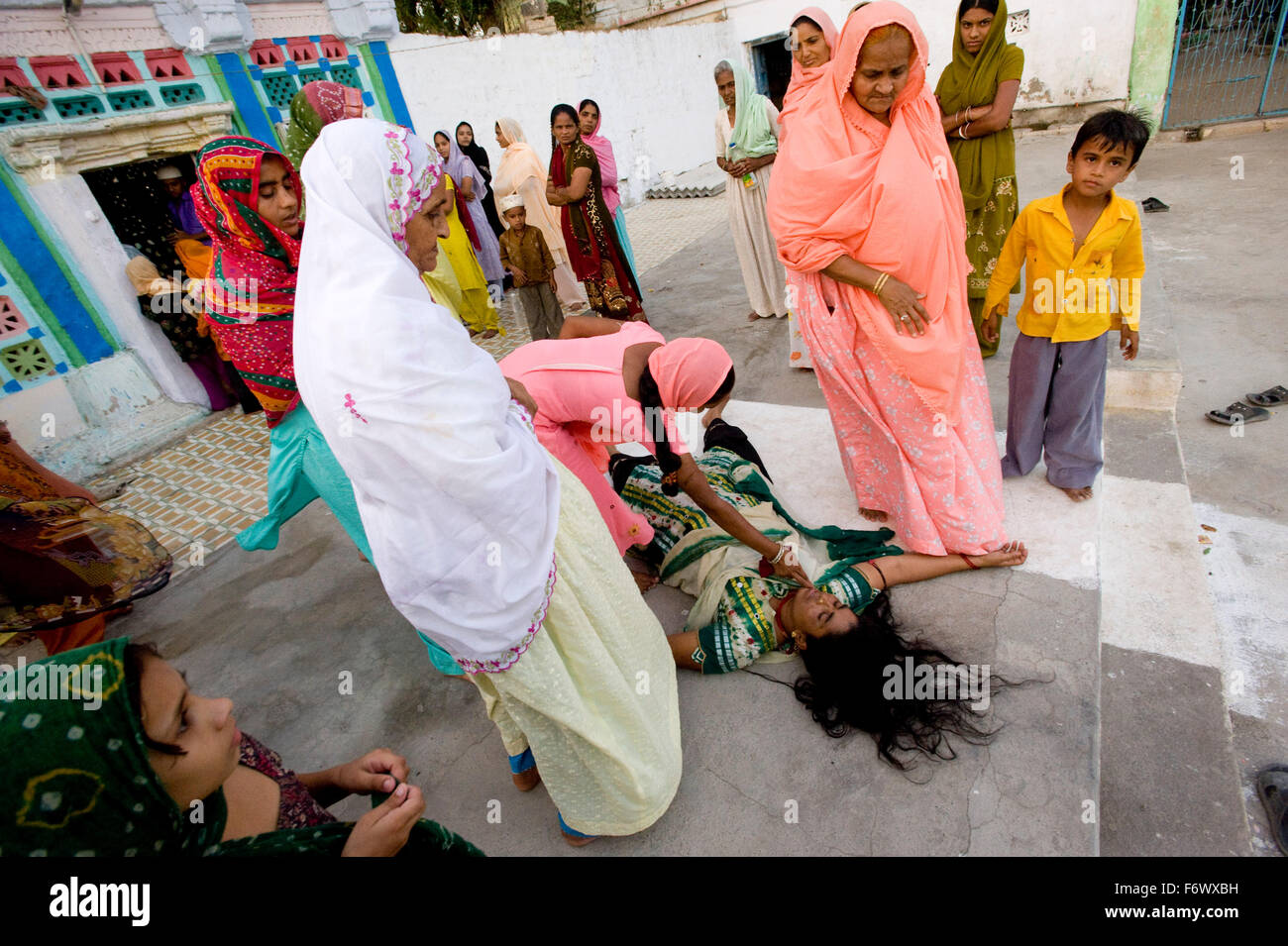 I membri della famiglia si radunano possedeva una donna che è crollato al di fuori del più piccolo dei santuari. Shah Shamshudin o Hayrat Shah Baba Dargah , n.a. , Gujarat. Foto Stock