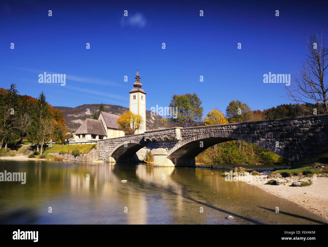 Soleggiata giornata autunnale sul lago di Bohinj nel Sloveniaa, con golden e alberi di arancio, blu cielo e acqua Foto Stock