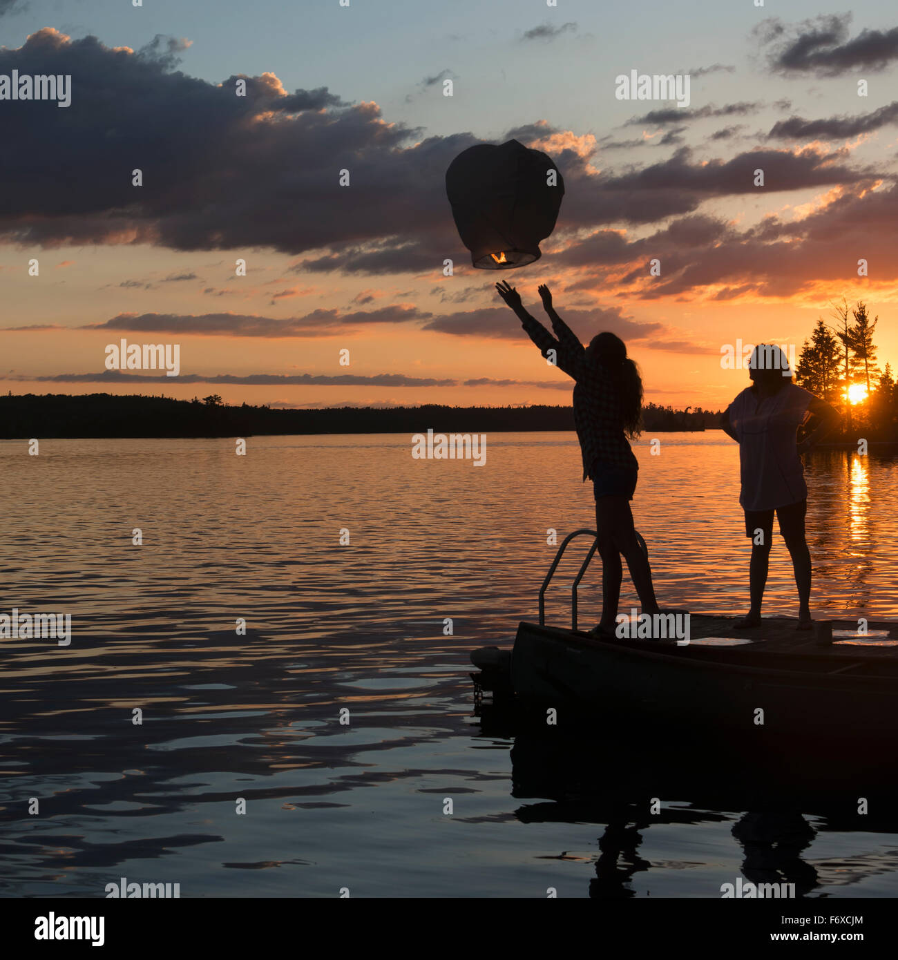 Silhouette di una ragazza adolescente rilasciando una lanterna accesa su un lago al tramonto; lago dei boschi, Ontario, Canada Foto Stock