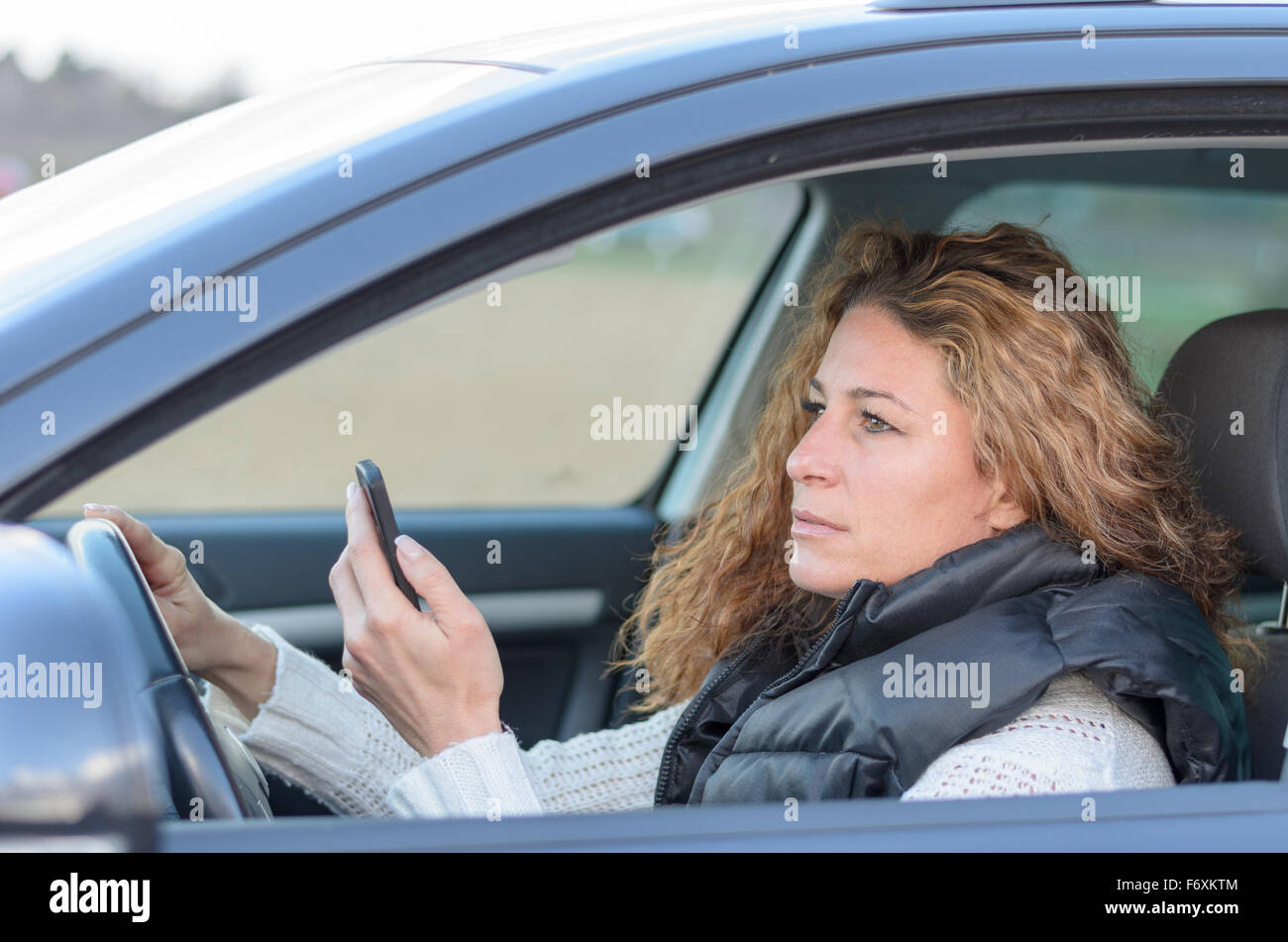 Donna ist la guida la sua automobile vand la lettura di un messaggio sul suo cellulare Foto Stock