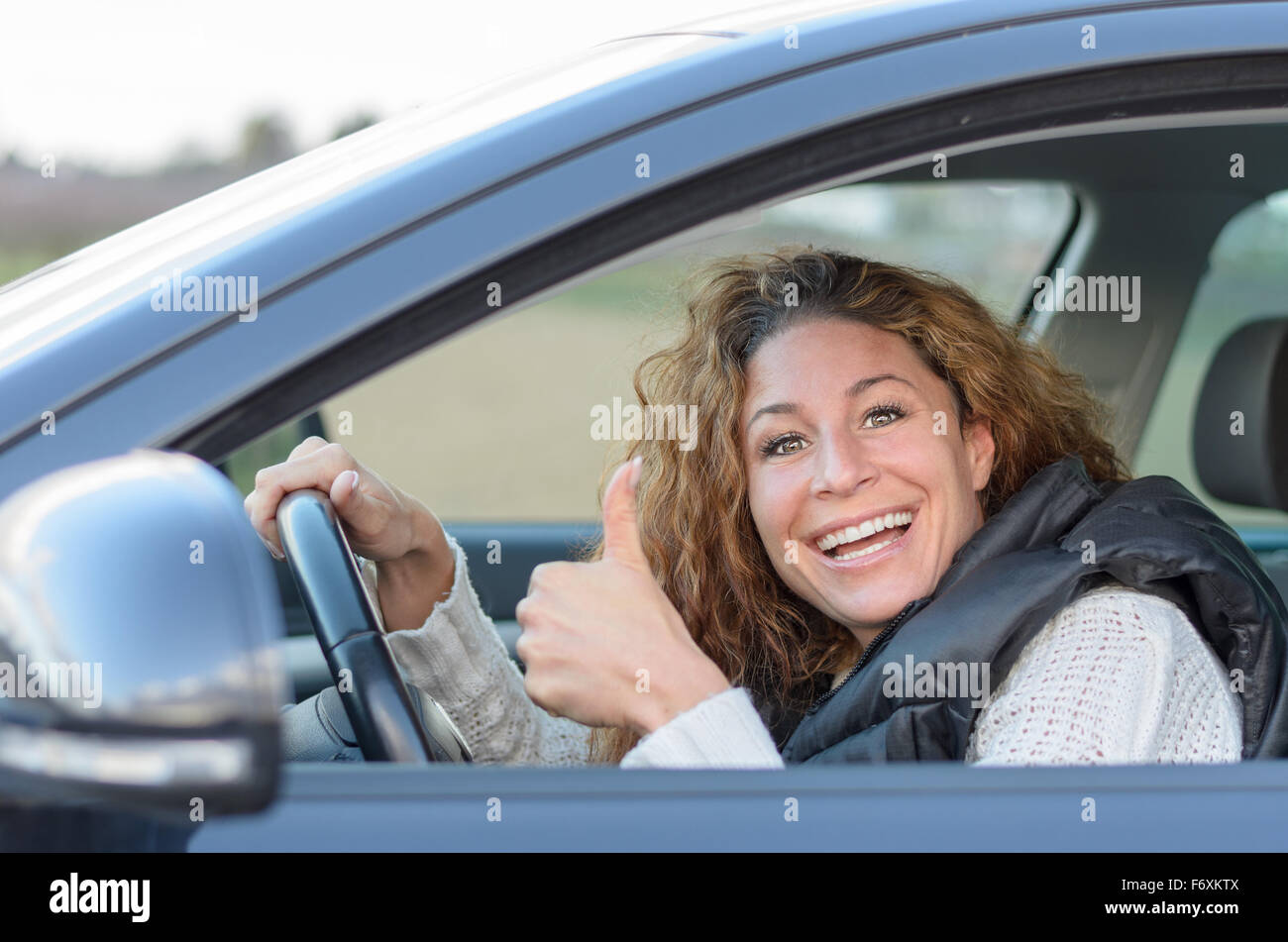 Donna alla guida la sua auto e dando un pollice in alto gesto Foto Stock