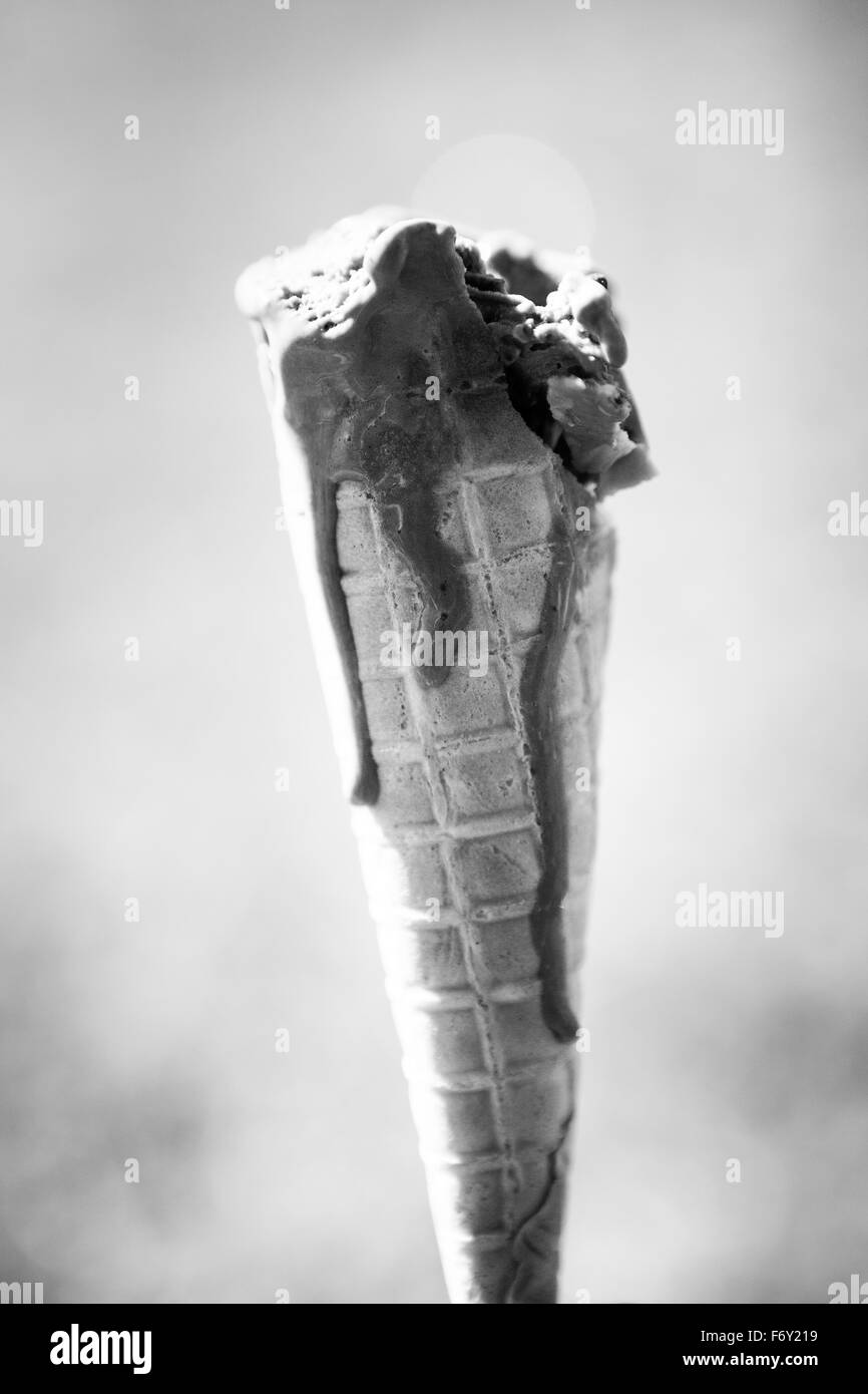 Singolo cono gelato con il gelato la fusione di lato verso il basso del cono in una calda giornata estiva contro un fuori fuoco erba bac Foto Stock