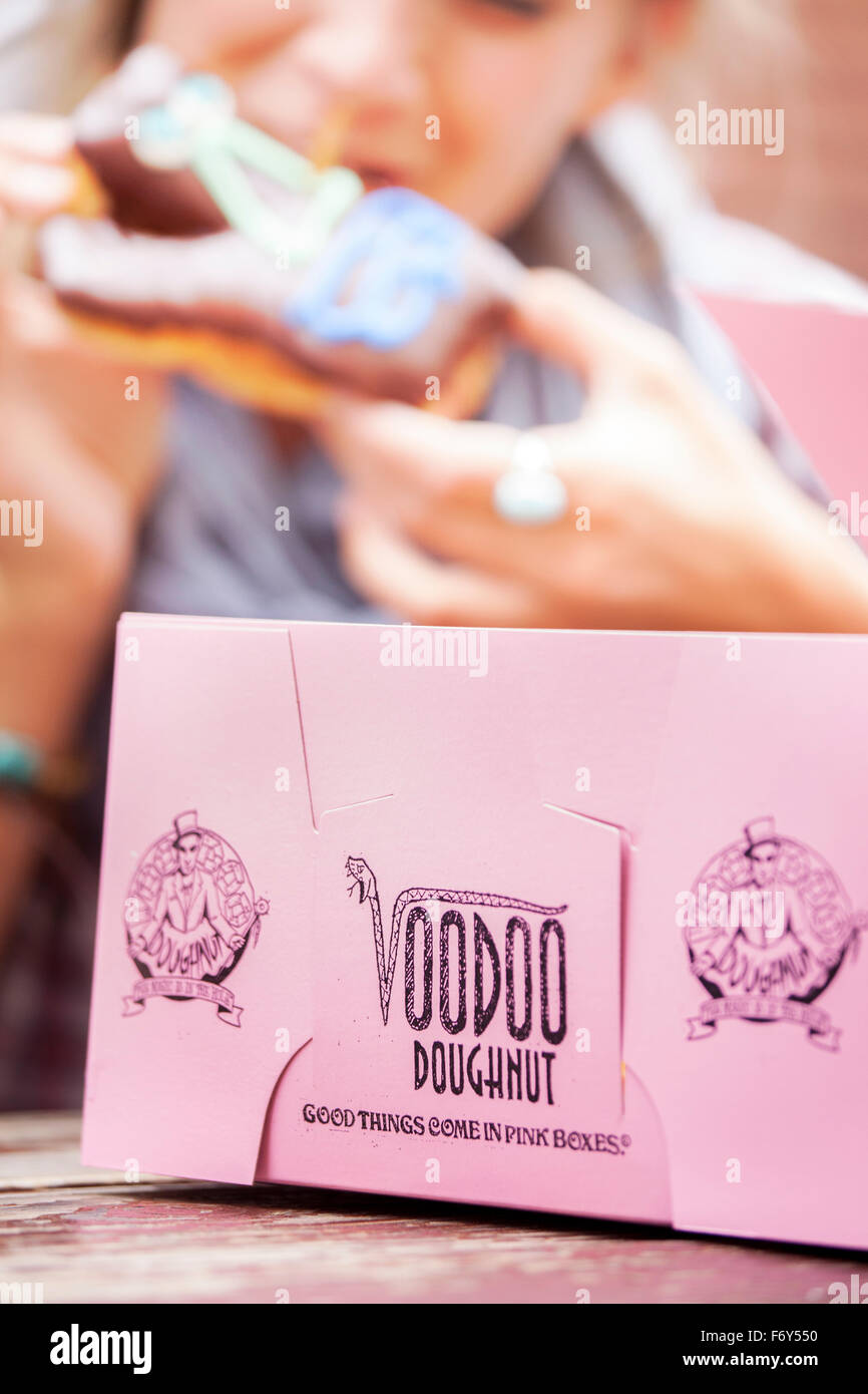 Una giovane donna si morde in una pasticceria di Voodoo Donuts a Portland, Oregon, dove 'Le Buone cose vengono in scatole rosa'. Foto Stock