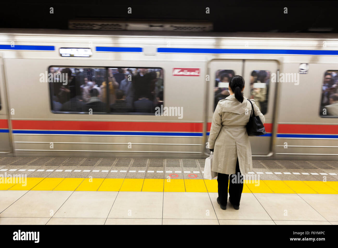 Una donna giapponese in attesa presso la metro per il passaggio di un treno Foto Stock