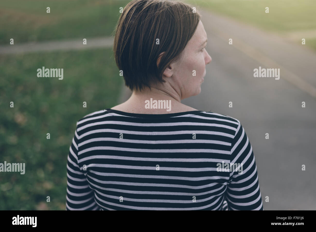 Da sola donna informale da dietro a piedi giù per la strada vuota sul pomeriggio autunnale e guardando al suo fianco, dai toni rétro con immagine Foto Stock