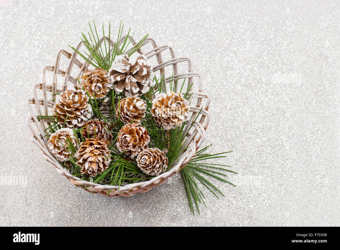 Coperta di neve pigne in legno ciotola di vimini su sfondo lucido Foto Stock