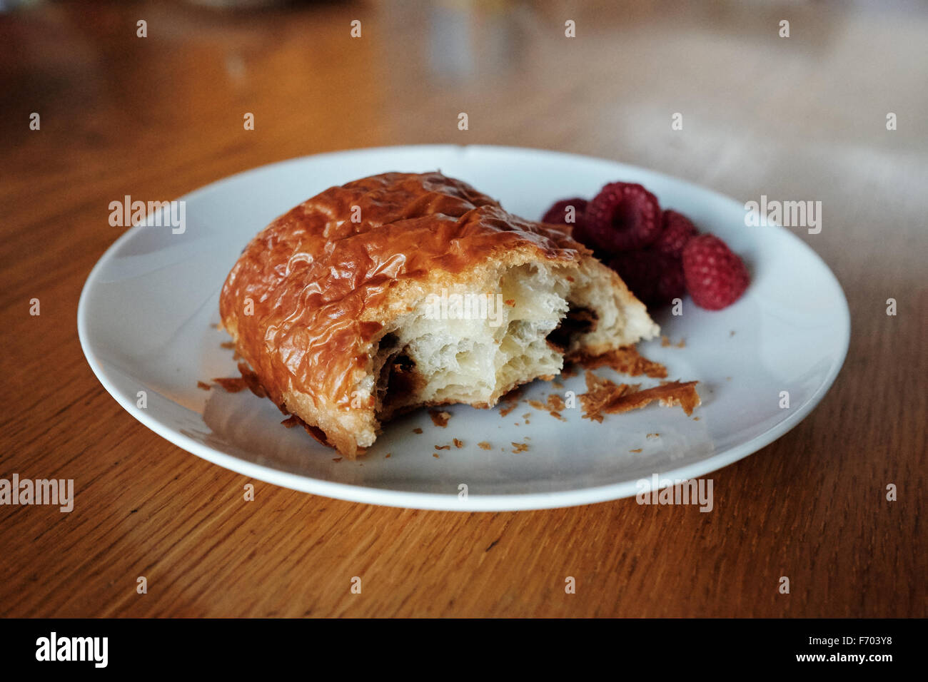 Pain au chocolate con il morso prese su una piastra mentre con lamponi Foto Stock