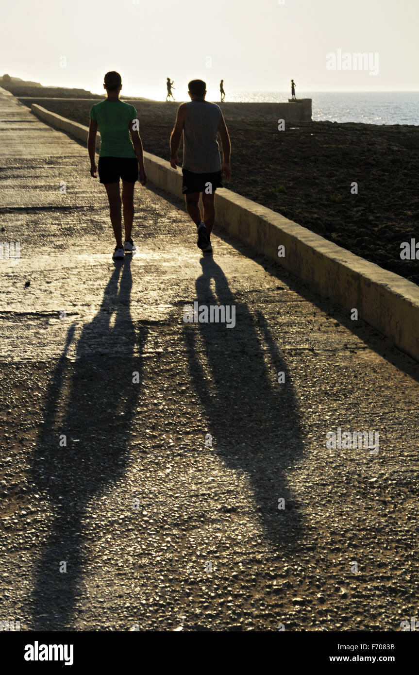 La gente camminare su una passeggiata sul mare al tramonto nella costa nord di isola di Gozo, Malta Foto Stock