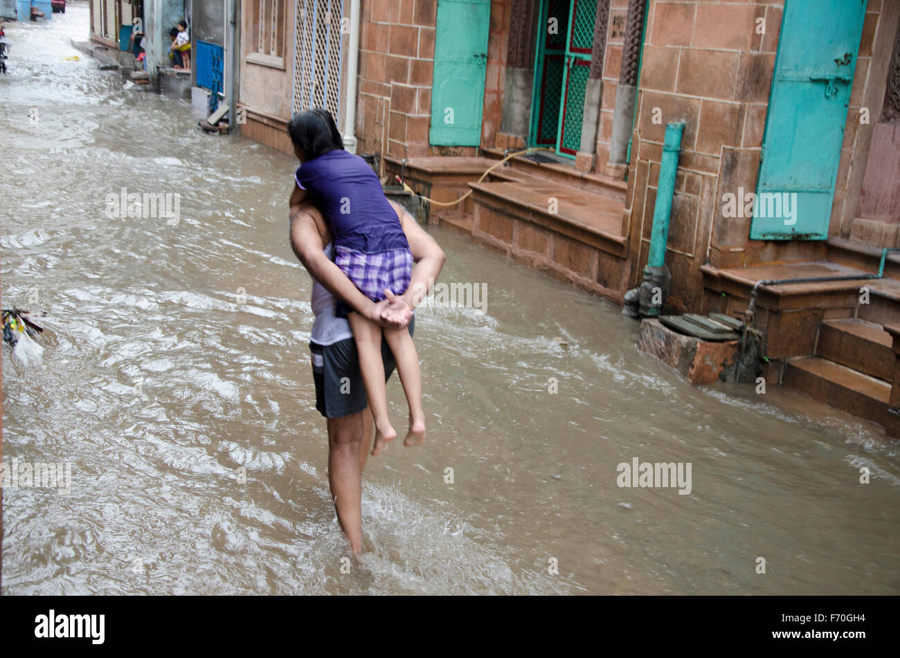 Uomo che porta la figlia sul retro acqua di pioggia sulla strada, Jodhpur, Rajasthan, India, Asia Foto Stock