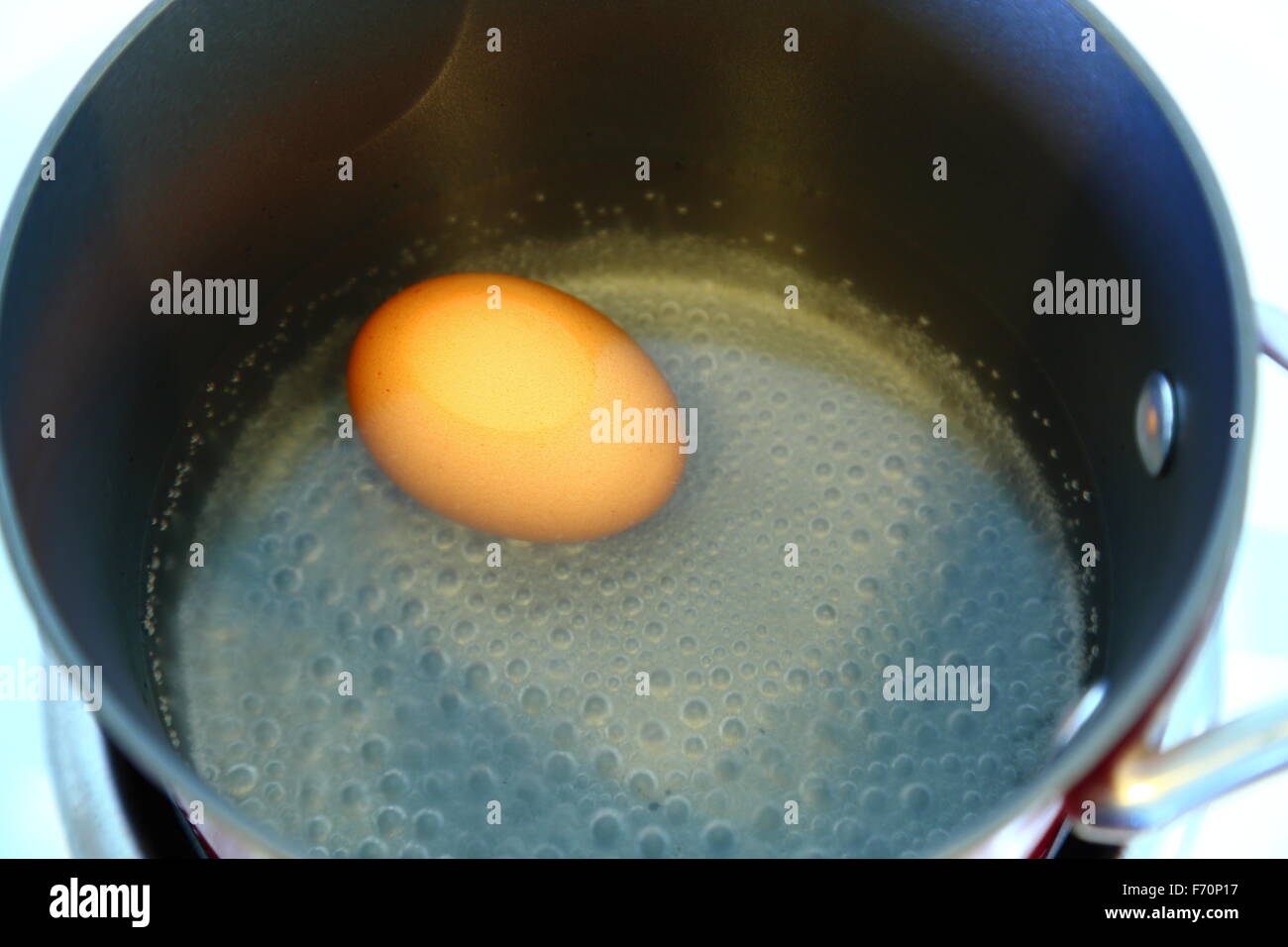 Un uovo ebollizione in una pentola di rosso su un fornello, visto dall'alto. Foto Stock