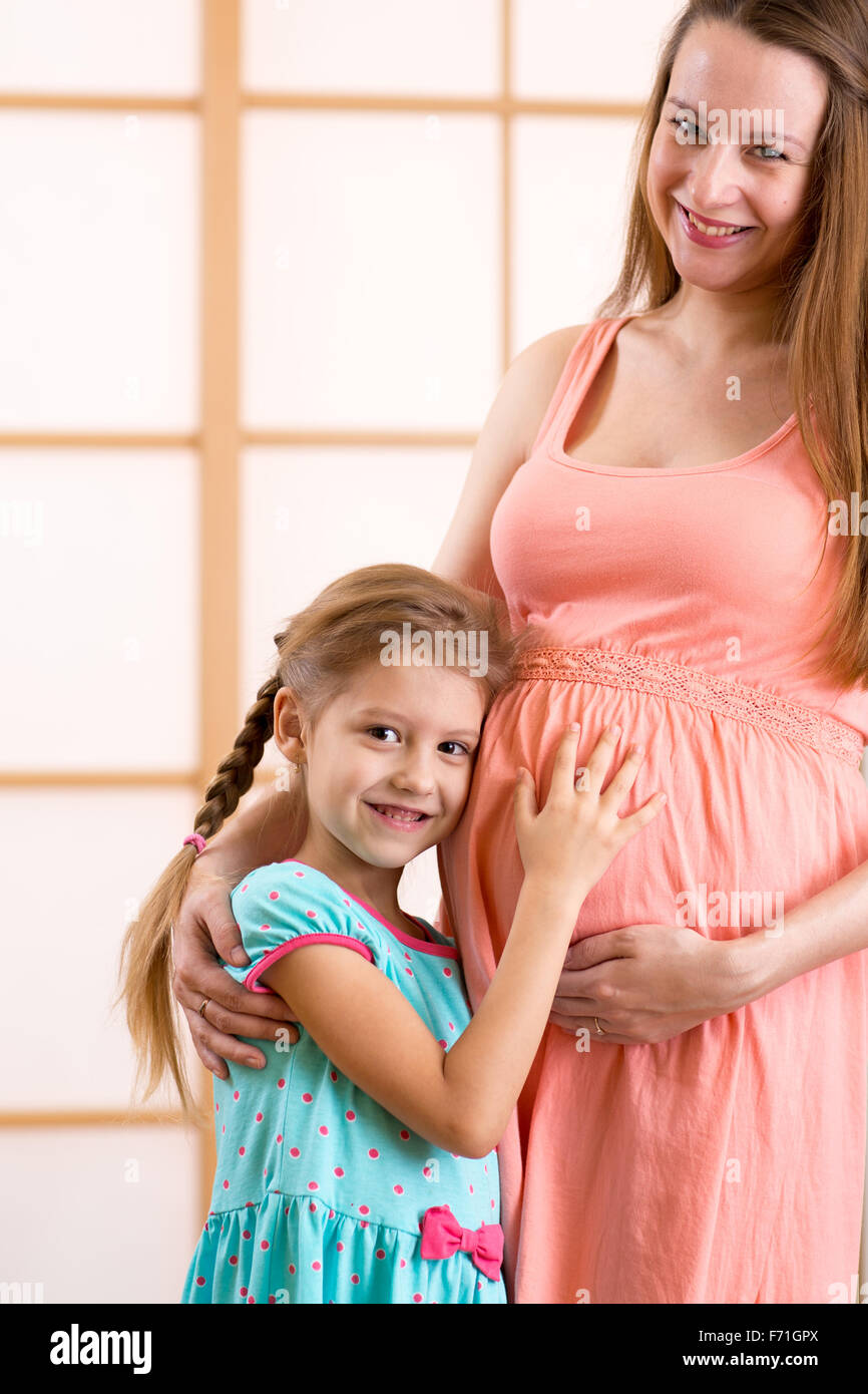 Capretto felice ragazza abbracciando in stato di gravidanza della madre ventre Foto Stock