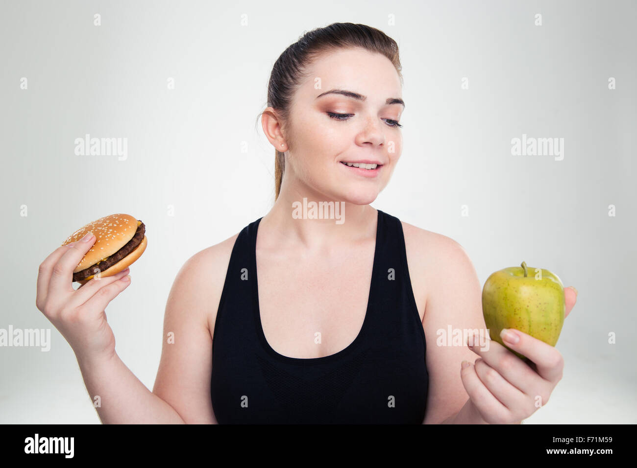 Ritratto di un felice donna grassa scegliendo tra burger o apple isolato su uno sfondo bianco Foto Stock