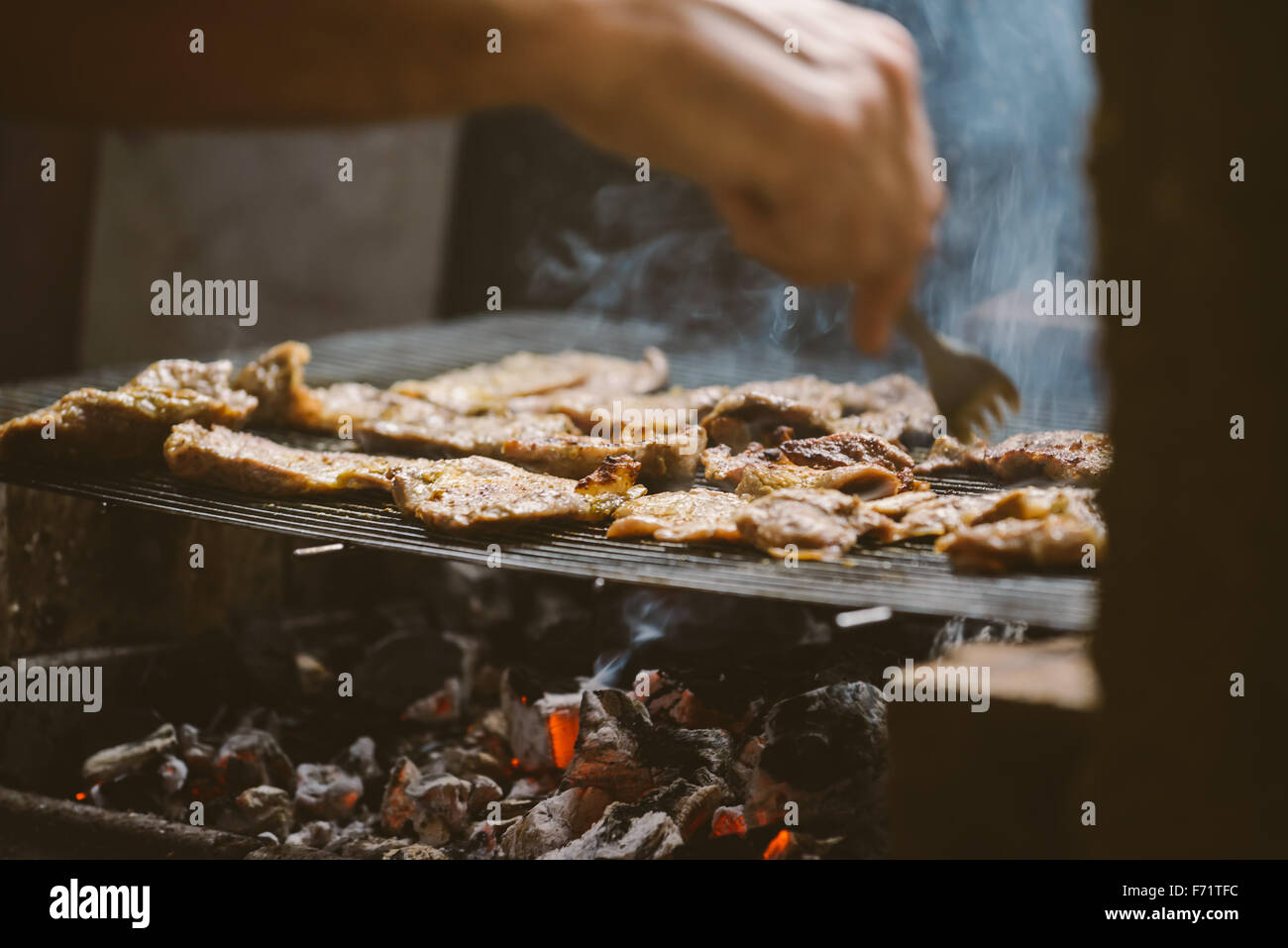 L uomo per grigliare carne di maiale braciole sul barbecue, luce naturale, dai toni retrò, messa a fuoco selettiva con profondità di campo ridotta. Foto Stock