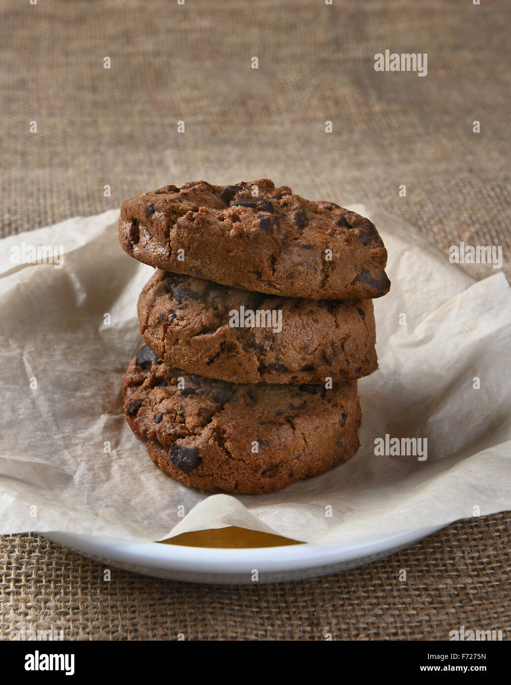 Vista dettagliata del cioccolato tre biscotti con scaglie di cioccolato su una piastra. Il delizioso sfornato fresco tratta e la piastra sono su una tela tabella c Foto Stock