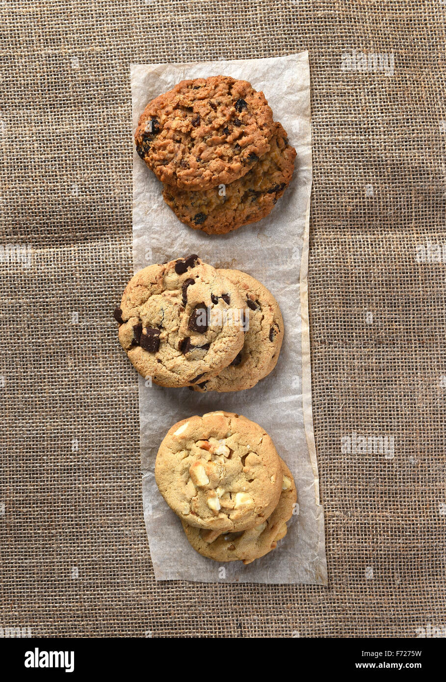 Angolo di alta vista di tre piccole pile di sfornato fresco holiday cookie su una striscia di carta pergamena su tela coperti da tavola. Foto Stock