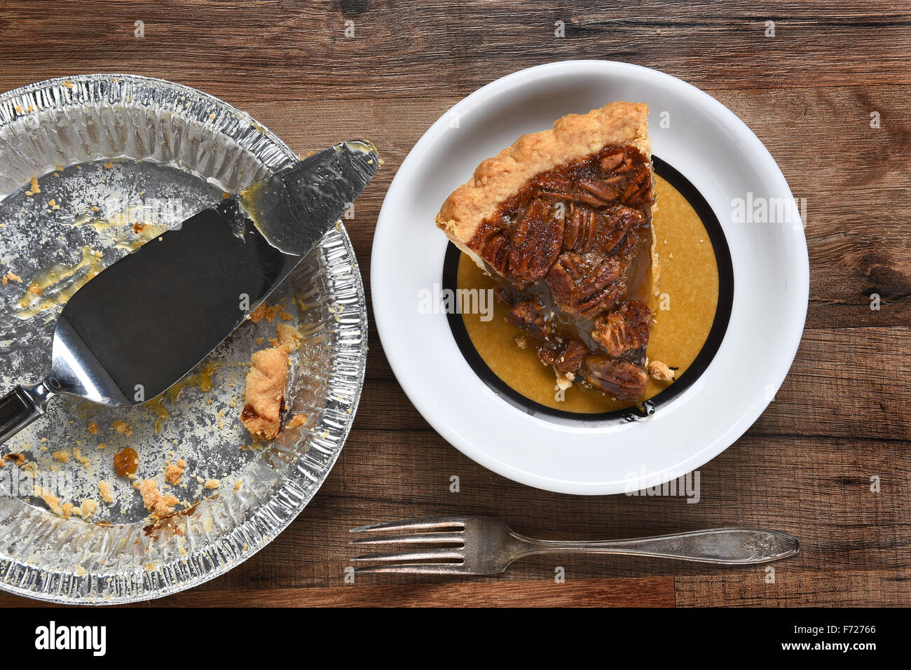 Angolo di alta vista di una fetta di torta alle noci pecan su una piastra accanto al vuoto ruoto con il server di . Su una tavola di legno con la forcella. Foto Stock