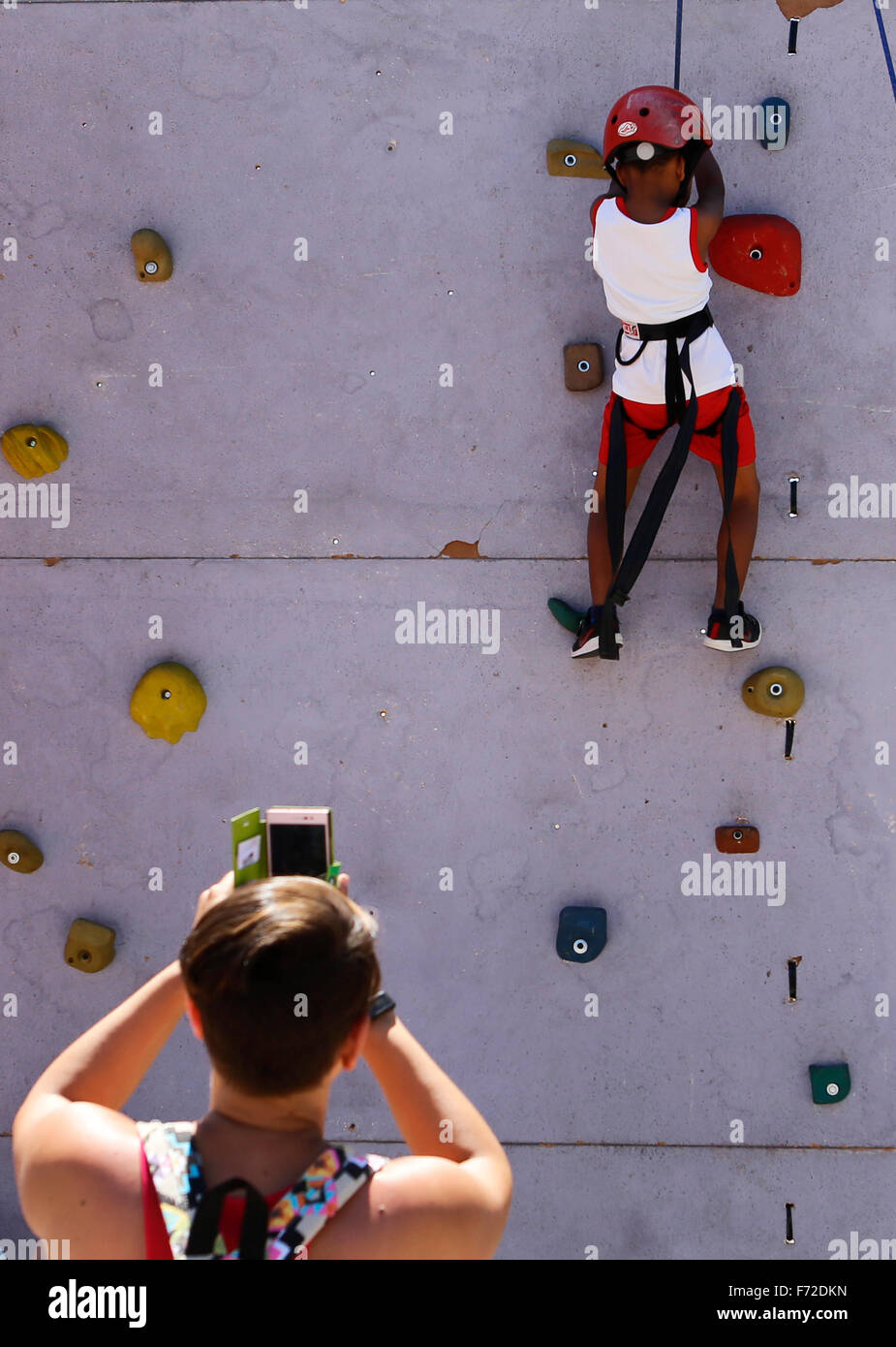 Un bambino che impara ad arrampicarsi su di una parete di arrampicata mentre sua madre le foto di lui nel corso di una gioventù locale sport fair di Palma. Foto Stock