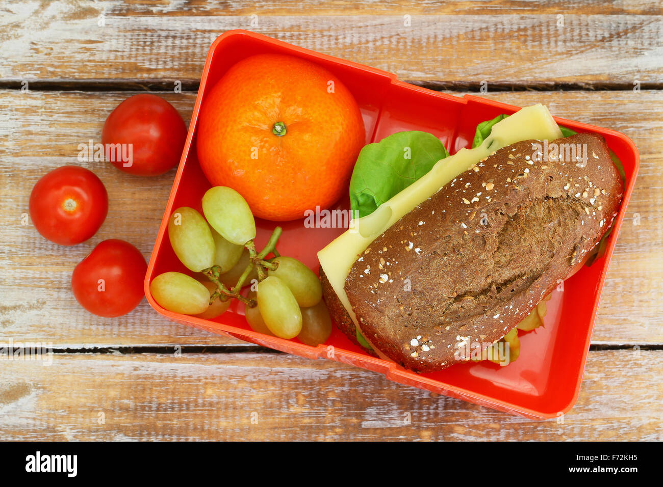 Scuola di sano scatola di pranzo con pane marrone sandwich di formaggio, mandarino, uva e pomodorini Foto Stock
