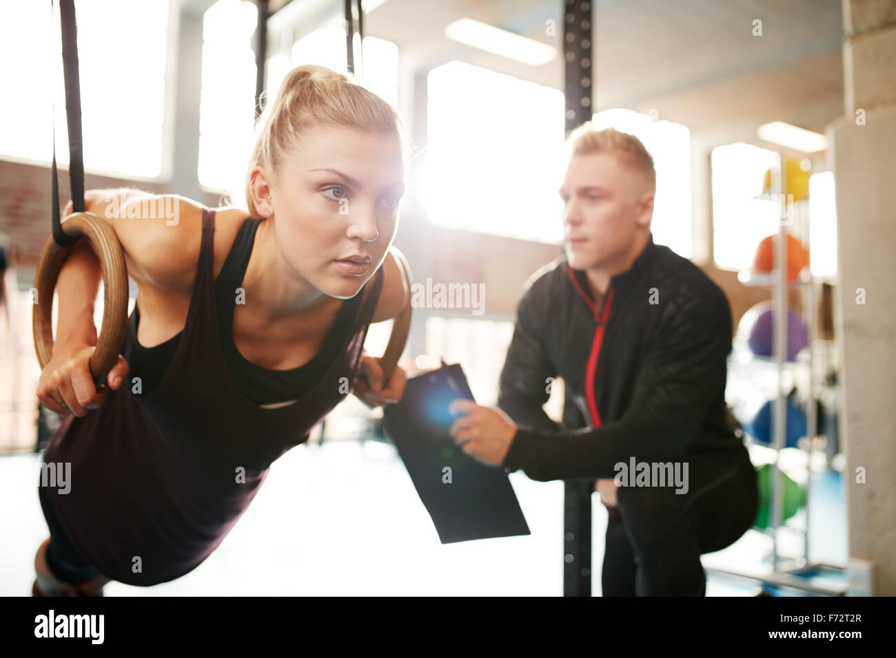 Montare la giovane donna con il suo personal fitness trainer in palestra esercizio con anelli di ginnastica Foto Stock