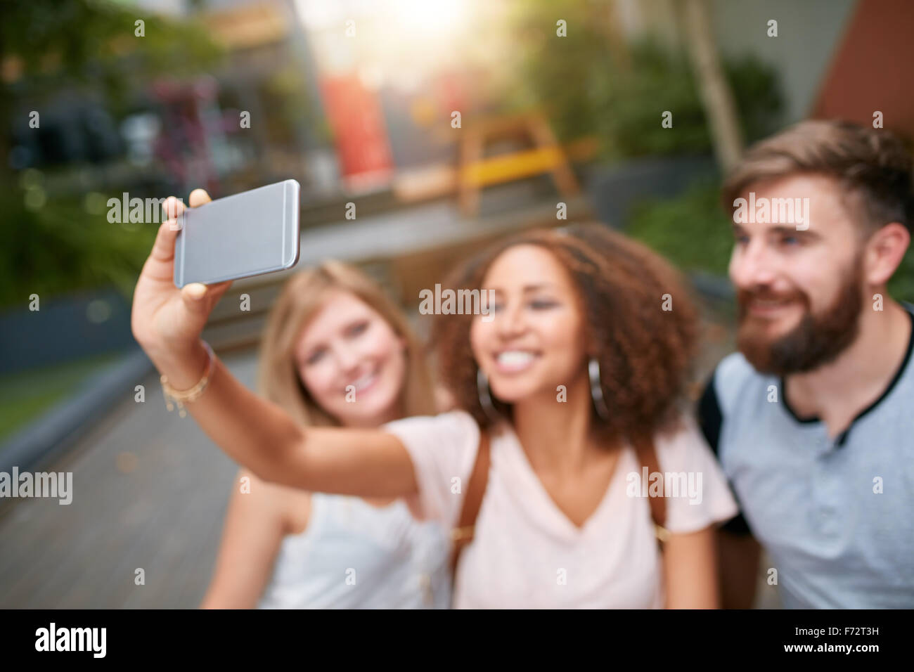 Colpo all'aperto della giovane donna prendendo autoritratto su telefono cellulare con i suoi amici. Tre giovani amici prendendo un selfie con smar Foto Stock
