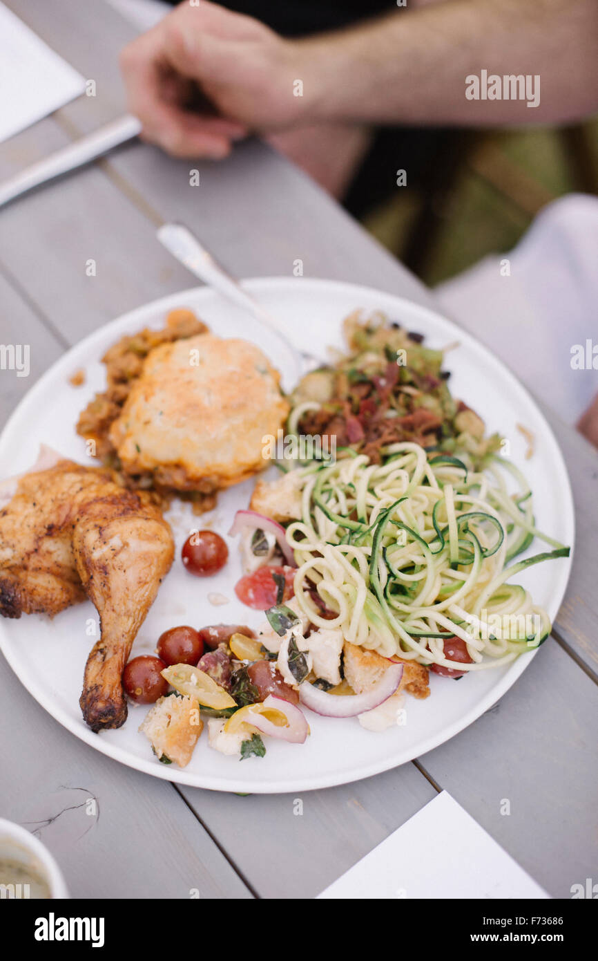 Il cibo sulla piastra ad una festa in giardino, pollo alla griglia e insalate. Foto Stock