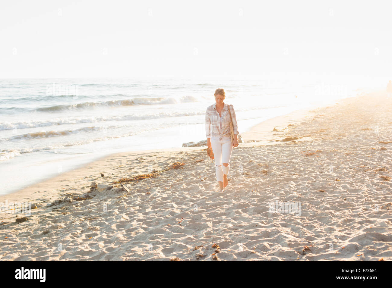 Donna che cammina lungo una spiaggia di sabbia in riva all'oceano. Foto Stock