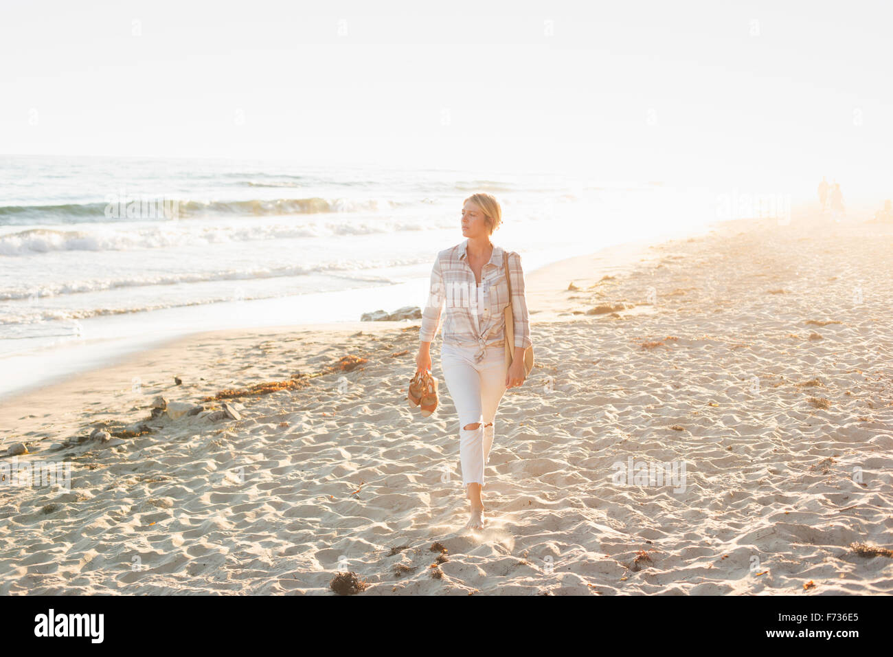 Donna che cammina lungo una spiaggia di sabbia in riva all'oceano. Foto Stock
