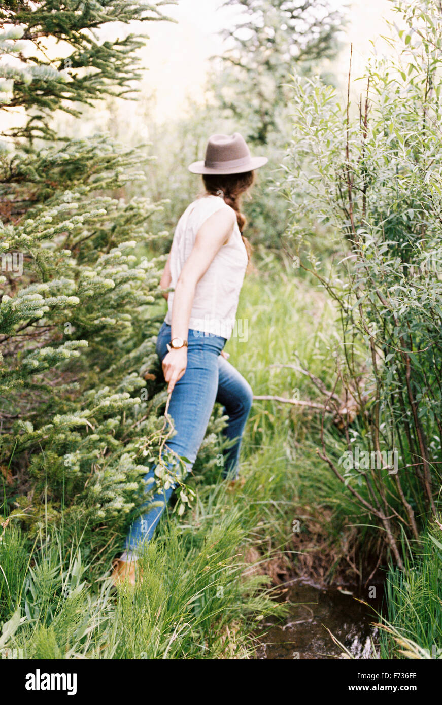Donna che indossa jeans e un cappello a piedi attraverso una foresta. Foto Stock