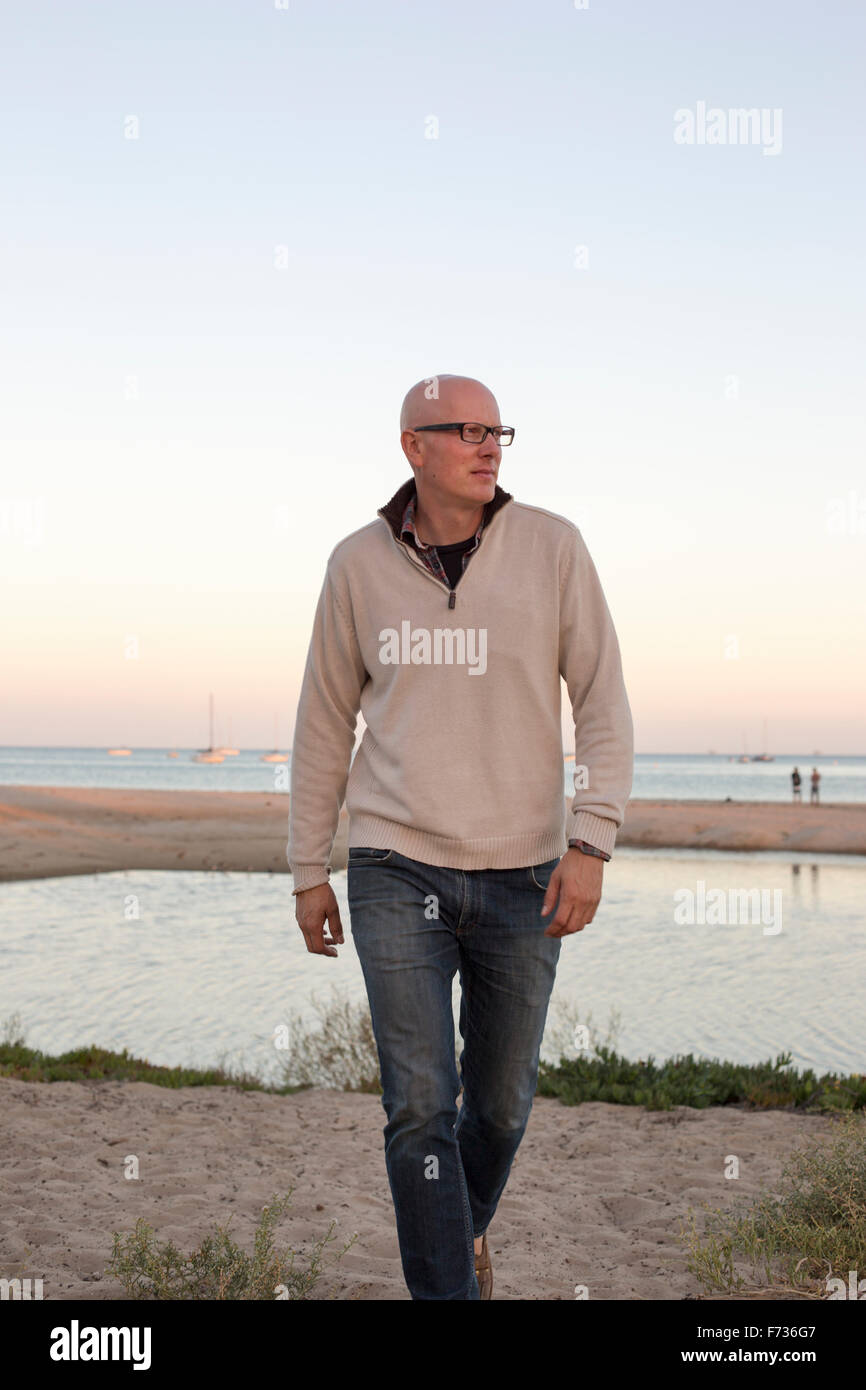 Bald uomo a camminare su una spiaggia di sabbia in riva all'oceano. Foto Stock
