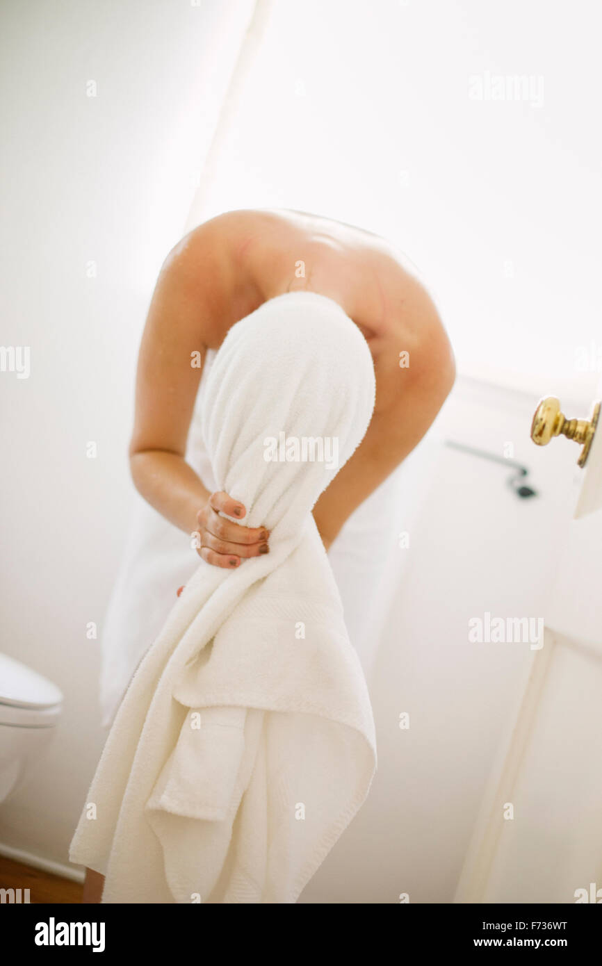 Donna avvolta in un asciugamano bianco in piedi in un bagno, avvolgendo i capelli in un asciugamano. Foto Stock