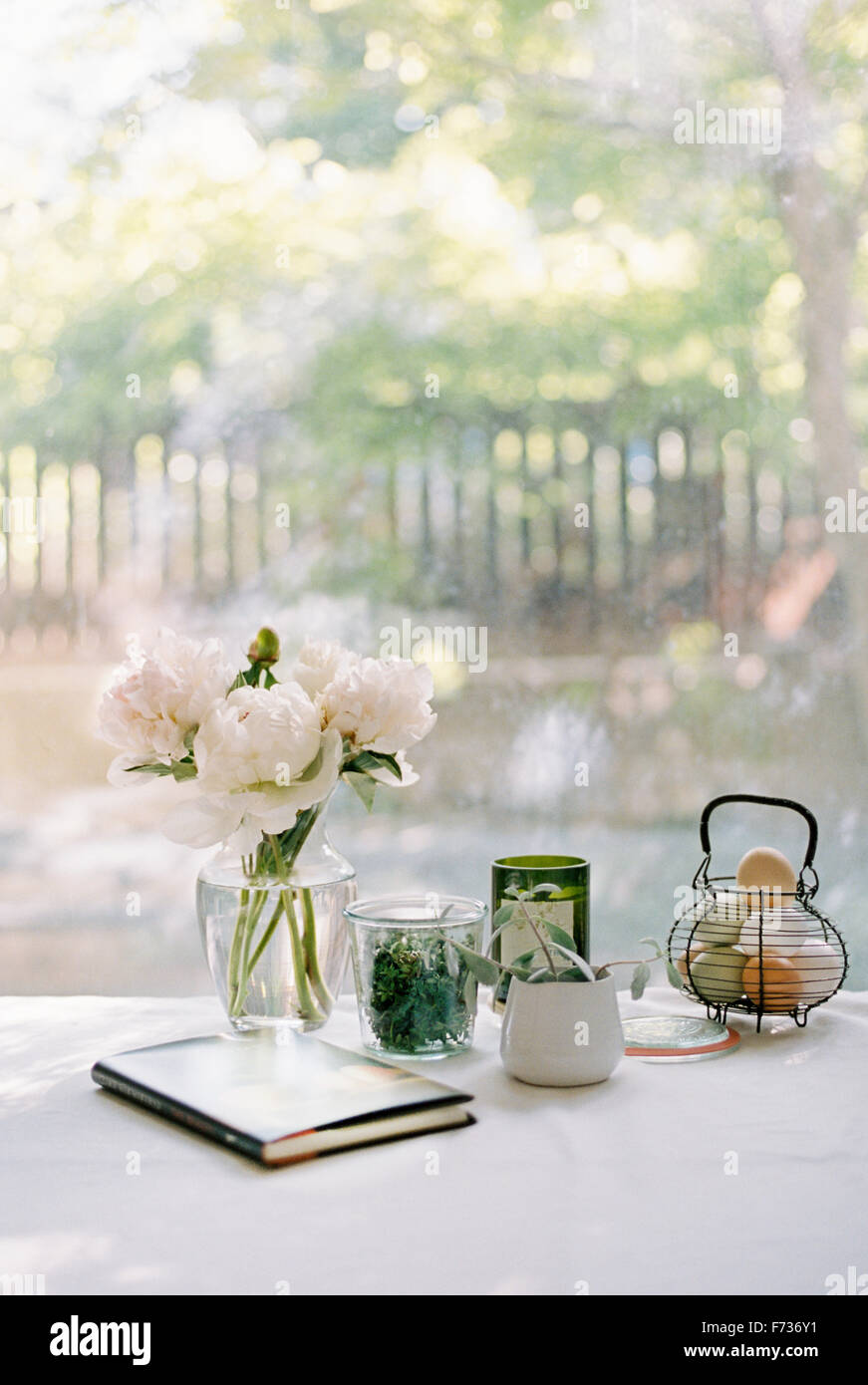 Vaso con rose bianche, notebook e vasi con erbe aromatiche e una cesta di uova fresche. Foto Stock