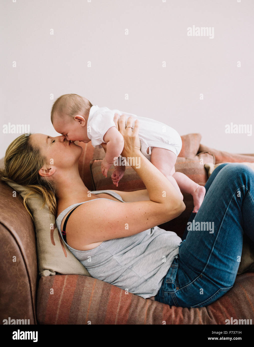 Una donna sdraiata su un divano a giocare con una bambina, bacio sulla guancia. Foto Stock