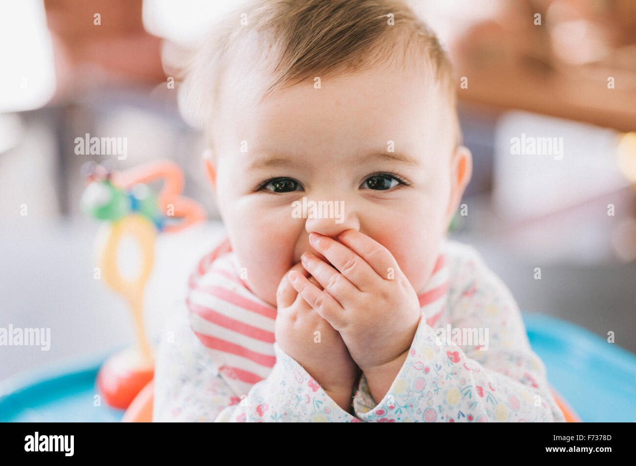 Una bambina con le mani che coprono la sua bocca, guardando la telecamera. Foto Stock